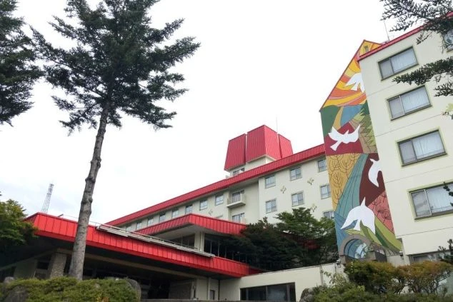 赤い屋根と壁に鳩や山々の絵が描かれたカラフルな壁画が特徴的な、大きな鷲ヶ岳のホテルの外観画像。リゾートバイトで、働く職場をイメージ