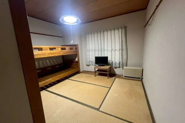 リゾートバイトの寮の相部屋。木製の二段ベッドがあり、テレビとテレビ台が置かれている。
