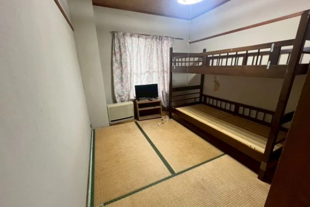 リゾートバイトの寮の相部屋。木製の二段ベッドがあり、テレビとテレビ台が置かれている。