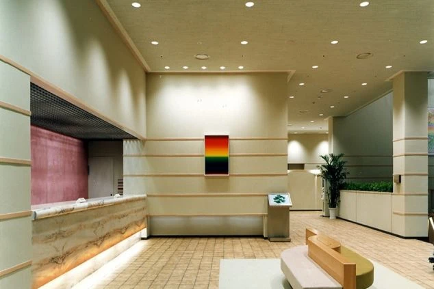明るい照明が灯るホテルのロビーと、左手には大理石調のフロントカウンター、奥の壁にはカラフルな抽象画が飾られているホテルの中の画像。