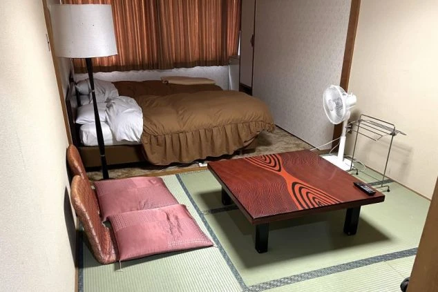 畳敷きのスペースとカーペット敷きのスペースがあるリゾートバイトの寮。奥にはベッドとフロアランプが見える。