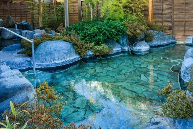 自然の岩と木々に囲まれた露天風呂。透明感のある温泉の湯面に空が映り込んでいる。