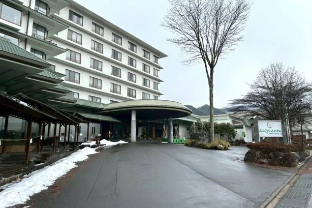 雪が残る路面の先に建つ、白い外壁と緑色の屋根が重なる多層階の大型ホテルの外観。円形の大きな車寄せがある。