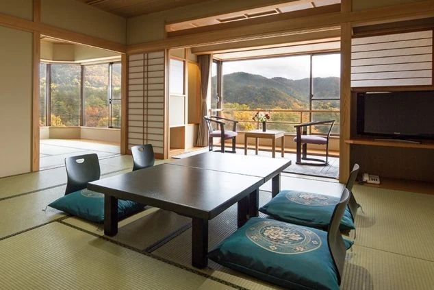 風光明媚な景色を一望できる、広々とした和室の客室。座卓と座布団、窓際にはテーブルセットが配置されている。