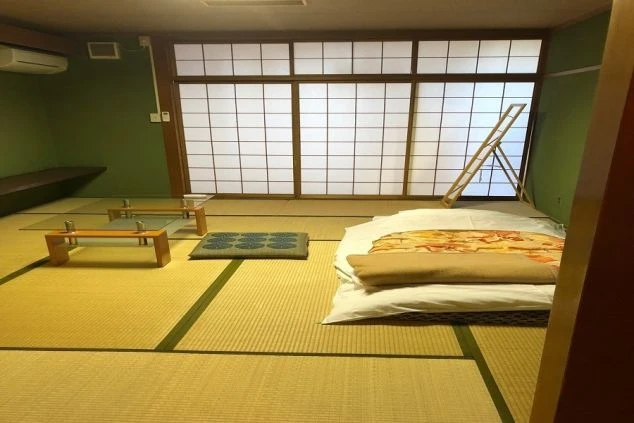 畳敷きの和室に、敷かれた布団とガラスのテーブルが置かれている画像。奥には大きな障子窓があり、全体的に和の趣を感じさせるリゾートバイトの個室寮の寝室のイメージ。