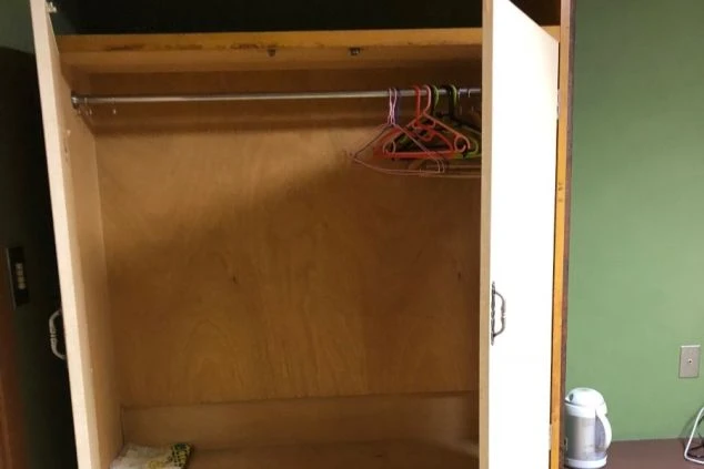 扉が開いた木製のクローゼットの中が写っている画像。ハンガーが数本かけられている。リゾートバイトの寮に備え付けられた、衣類を収納できるクローゼットのイメージ。
