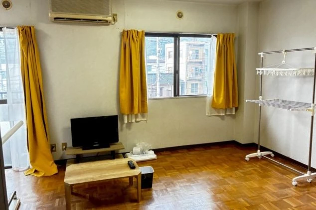 リゾートバイトの寮の居室。テレビ、エアコン、物干しがあり、奥には大きな窓がある。