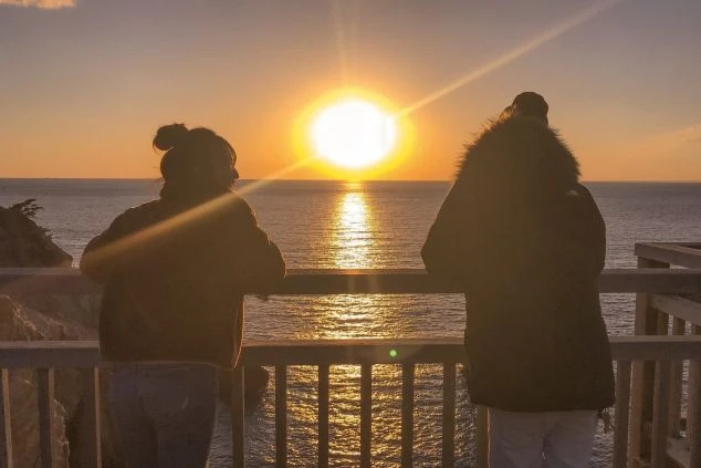 海に沈む夕日を眺める2人の人物のシルエット。オレンジ色に輝く水面が美しい。