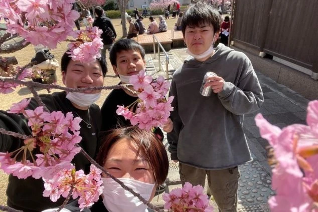 満開の桜の下で、笑顔を見せる4人の友人たち。春の陽気を感じさせる楽しげな一枚。