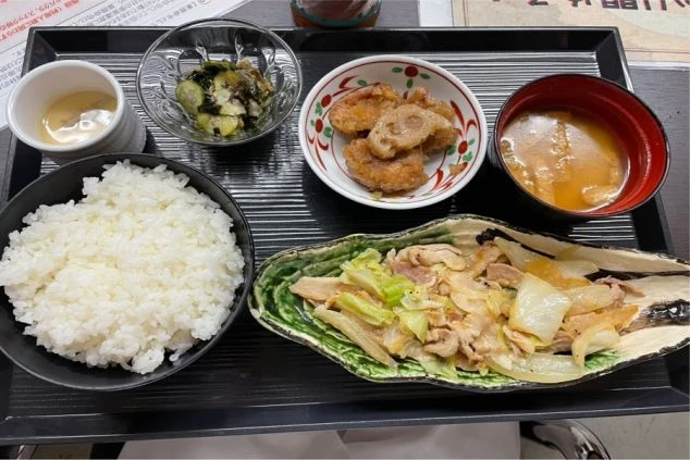 白いご飯、豚肉とキャベツの味噌炒め、小鉢の和え物、鶏肉の唐揚げ、味噌汁、茶碗蒸しが並んでいるリゾートバイトの賄いの画像。