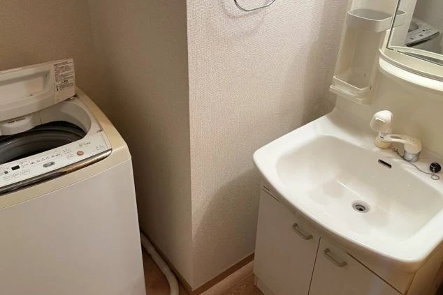 リゾートバイトの寮の洗面所の画像。洗面台の隣に洗濯機が置かれている。リゾートバイトの寮の設備の画像。