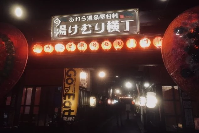 提灯が並び「あわら温泉屋台村 湯けむり横丁」と書かれた看板が光る、夜の温泉街の入り口が写っている画像。福井県あわら温泉でリゾートバイトする場所のイメージ