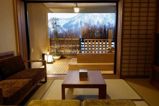 窓の外に雪景色が広がる、和室の客室の画像。部屋には座卓とソファが置かれ、窓の外には露天風呂が見える。リゾートバイトの寮やホテルの客室の画像。