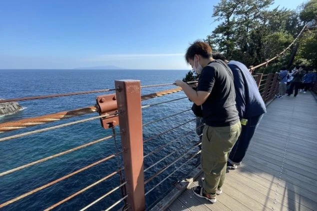 リゾートバイトの牛行先から車で10分程度のところにある城ヶ崎海岸の門脇つり橋から、男性二人が海を見下ろしている画像。休日の過ごし方のイメージ。