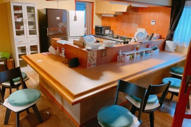 リゾートバイトの個室寮の共用キッチンの画像。L字カウンターになっており、6つの椅子が並べられている。