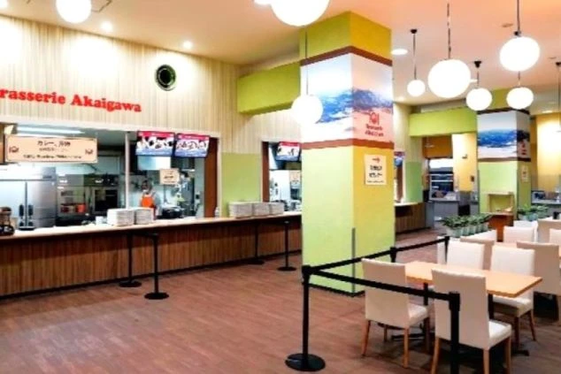 スキー場内にあるフードコートのようなレストランの画像。料理提供カウンターと、奥にはテーブル席が広がり、食事を提供するスタッフのイメージ。