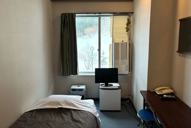 館内男子寮の室内写真。TVやベッド、窓、暖房器具があり快適な環境。