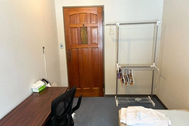 館内の男子寮の写真。木製のドアに物干しラック、デスクと椅子が写っている。