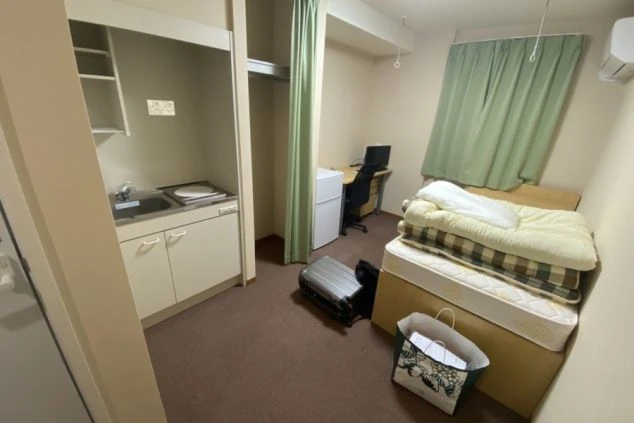 リゾートバイトの寮の個室の画像。ベッド・キッチン・冷蔵庫・デスク・チェア・エアコンが見える。