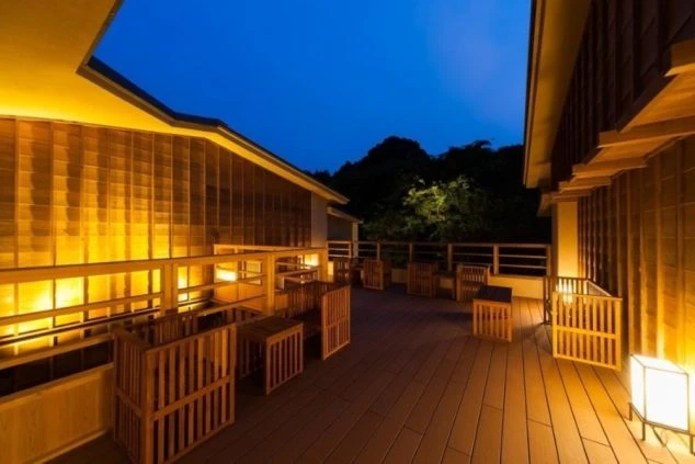 夜の屋外テラスの画像。木製のテーブルと椅子が並び、間接照明が温かく空間を照らしている。旅館やホテルの落ち着いた雰囲気のテラスのイメージ。