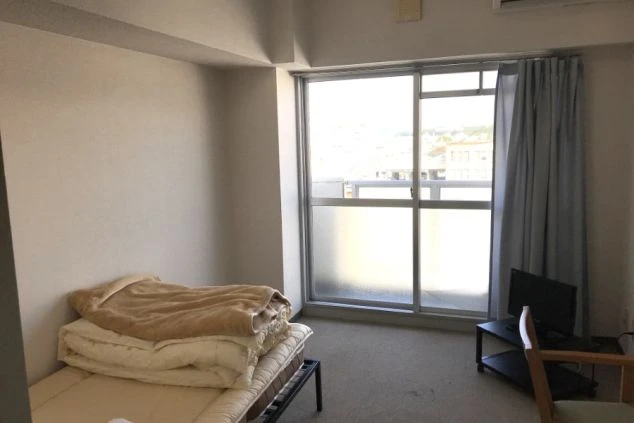 ベッドと布団が置かれたリゾートバイトの個室寮の画像。窓からは外の景色が見え、テレビも備え付けられている。