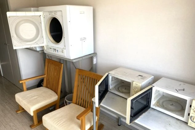 電子レンジと乾燥機、木製の椅子が置かれたリゾートバイト寮の共用スペースの画像。