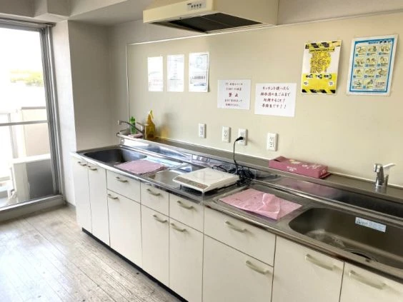 明るく清潔な共用キッチンの画像。シンクとIHクッキングヒーターがあり、壁には利用ルールが貼られている。リゾートバイトの寮の共有スペースのイメージ。