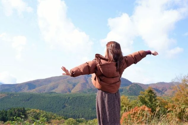 広がる山並みを背景に、両手を広げて深呼吸する女性。リゾートバイトで心身をリフレッシュするイメージ。