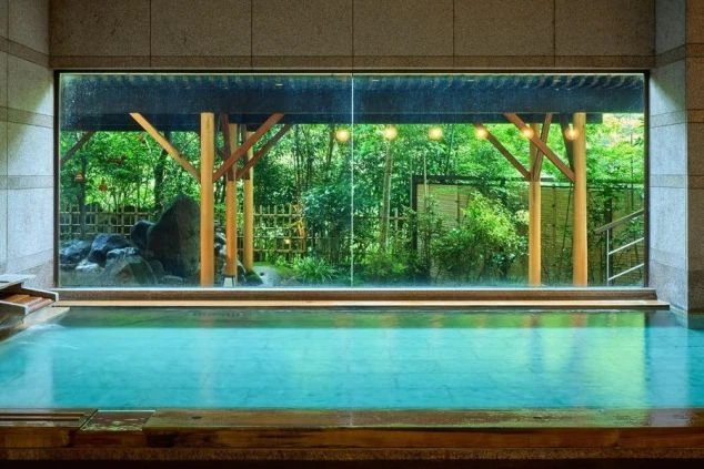 リゾートバイト就業先の大きな窓から緑が見える、開放的な温泉の湯船。リゾートバイトの癒し。