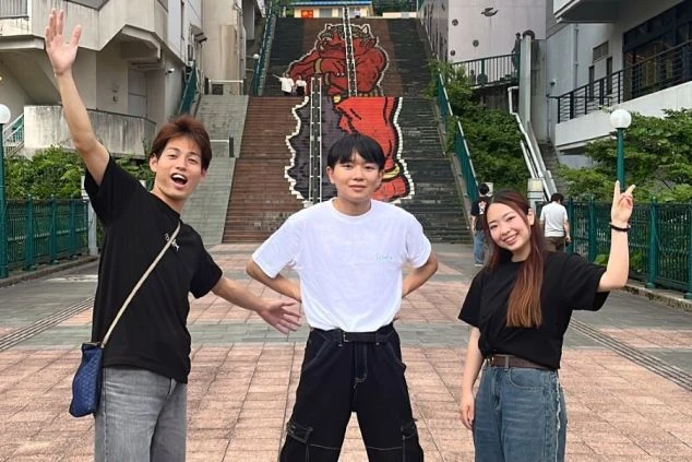 栃木県鬼怒川温泉の「ふれあい橋」の階段に描かれた巨大な赤鬼「鬼怒太」の前で、楽しそうにポーズをとる若者たち。リゾートバイトの仲間との思い出作りに。