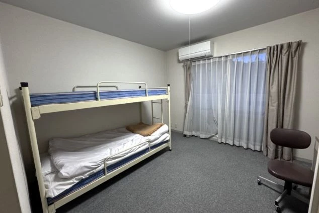 二段ベッドが置かれた寮の部屋。窓にはカーテンがかかっており、エアコンが設置されている。