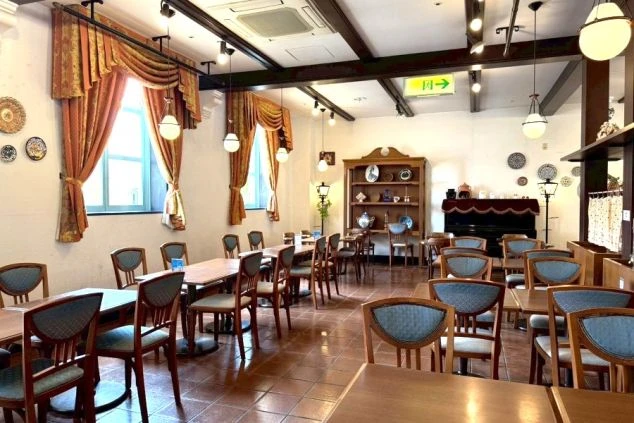 エレガントなドレープカーテンがかかる窓際や、壁に飾られた絵皿、クラシックな木製家具が並ぶ、落ち着いたスペイン風の装飾が施された空間です。