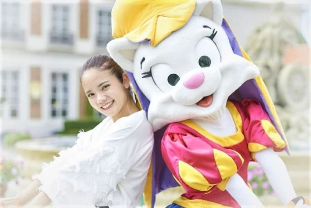 テーマパークでマスコットキャラクターと女性が笑顔で並ぶイメージ画像。リゾートバイトの休日を満喫。