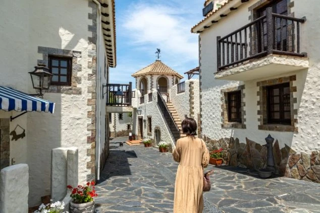 石畳の道を歩く女性。白い壁と瓦屋根のヨーロッパ風の街並みが広がるイメージ画像。リゾートバイトの休日を満喫。