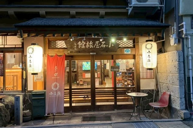 木造のレトロな建物で、正面には提灯や赤いのぼりが飾られ、窓からは暖かい光が漏れている。