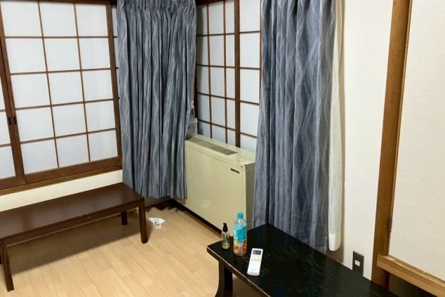 寮の和室。畳敷きの床にテーブル、ベンチ、暖房器具、障子が映る。