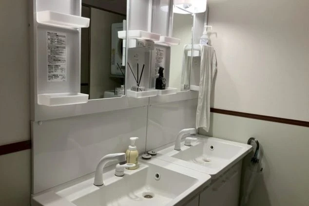 寮の洗面所。シンク、鏡、ボトル類が整頓された様子が映る。