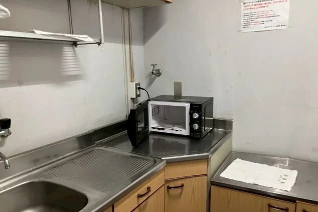 寮のキッチン。シンクと電子レンジ、作業台、壁の棚が映る。