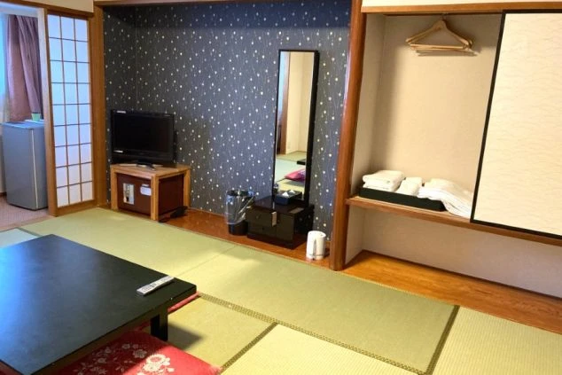 リゾートバイトの客室寮の和室の部屋の画像。黒い座卓と座布団が置かれ、収納スペースには布団が畳んで積まれている。リゾートバイトの寮の部屋の画像。