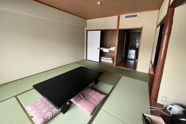 リゾートバイトの客室寮の和室の部屋の画像。黒い座卓と座布団が置かれ、収納スペースには布団が畳んで積まれている。リゾートバイトの寮の部屋の画像。