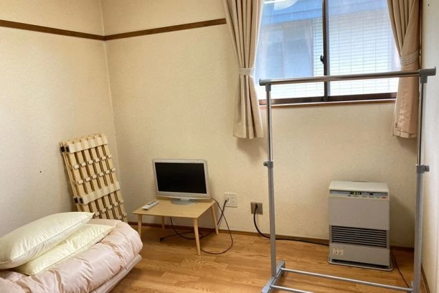 寮の個室。布団、テレビ、ハンガーラック、ストーブが映る。