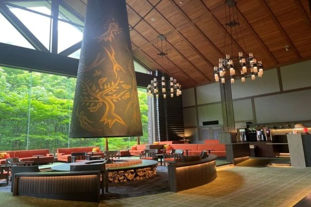 ホテルのロビー。巨大な暖炉と窓から見える森が特徴の豪華な空間が映る職場のイメージ画像。