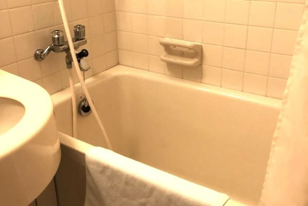 ユニットバスの浴槽。シャワーが備わっており、清潔感のある白いタイル壁。