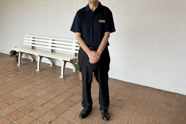 ポロシャツに黒のスラックス、黒の革靴を着用した男性フロントスタッフの制服画像。