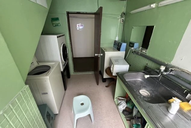 リゾートバイトの寮の共用スペースの画像。緑色の壁が特徴的な部屋に、洗濯機と乾燥機、流し台が設置されている。リゾートバイトの寮の共用スペースの画像。