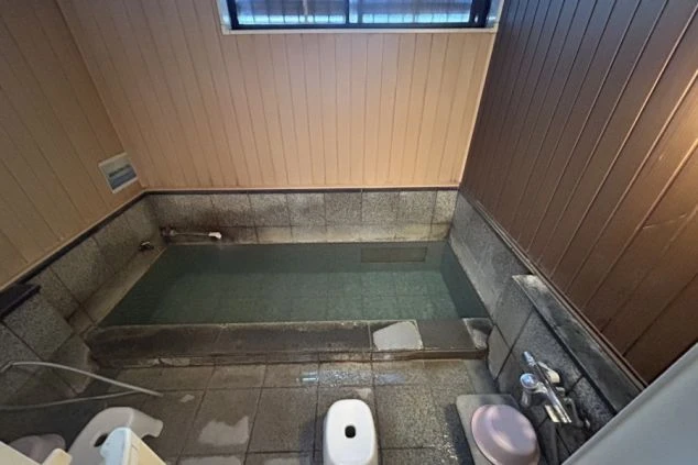 リゾートバイトの寮の共同風呂の画像。広い湯船と、洗い場には椅子と桶が置かれている。リゾートバイトの寮の風呂場の画像。