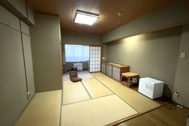 リゾートバイトの寮の部屋の画像。和風の畳の部屋に冷蔵庫や座椅子、収納棚が置かれており、落ち着いた雰囲気の部屋であることがわかる。リゾートバイトの寮の部屋の画像。