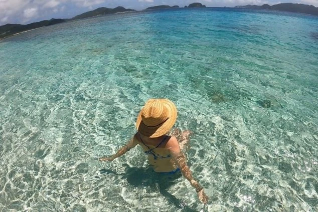 沖縄の透明度の高い海で水遊びをする女性。離島やビーチでのリゾートバイトで、仕事の合間に美しい海を満喫。マリンアクティビティや海の家での求人。