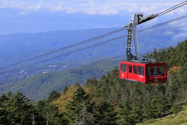 北八ヶ岳ロープウェイ。赤いゴンドラが緑豊かな山々の上を運航する絶景のイメージ画像。リゾートバイトの休日を満喫。