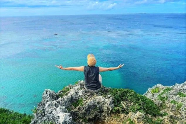 沖縄宮古島の断崖絶壁からエメラルドグリーンの海を眺める人物。両手を広げて開放感を表現。絶景の離島でリゾートバイト。ホテル、旅館、観光施設で働きながら、美しい自然を満喫できます。